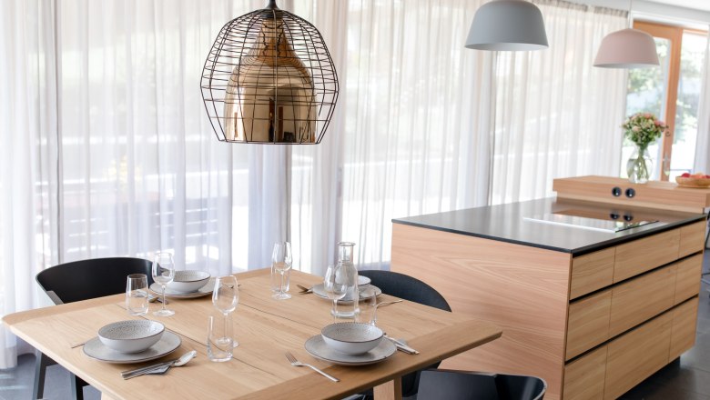 Dom pri jazere, © schwarz-koenig.at Moderná kuchyňa s dreveným stolom pre štyri osoby a kuchynským ostrovom v pozadí.