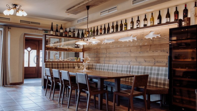 Tu sa cítite ako doma, © Niederösterreich Werbung/thecreatingclick.com Útulný jedálenský kút s dreveným stolom, stoličkami a lavicou, zdobený fľašami na víno a motívmi rýb na stene.