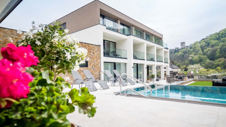 Dunajský strom © fotografia pfeffel, © © photography pfeffel Moderná budova s bazénom a ležadlami, obklopená zelenou krajinou a hradom v pozadí.