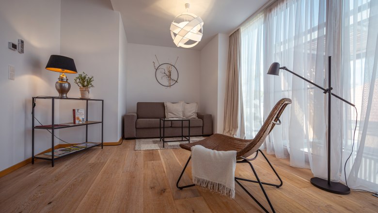 Apartmány Hausgnost, © Niederösterreich Werbung / Maximilian Pawlikowsky Moderne zariadená obývacia izba s pohovkou, kreslom, stojacou lampou a veľkým oknom so závesmi.