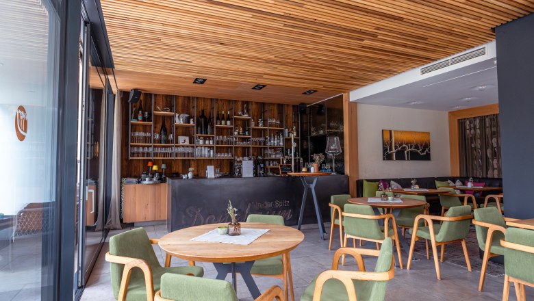 Boutique hotel WeinSpitz, © Niederösterreich Werbung / Maximilian Pawlikowsky Pohľad do interiéru vinárskeho salónika s drevenými prvkami, zelenými stoličkami a barom v pozadí.