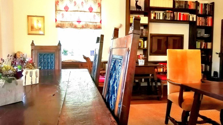 Raňajková miestnosť, © Landsitz Oberhof Útulná raňajková miestnosť s dreveným stolom, modrými stoličkami, policou na knihy a ozdobným oknom.