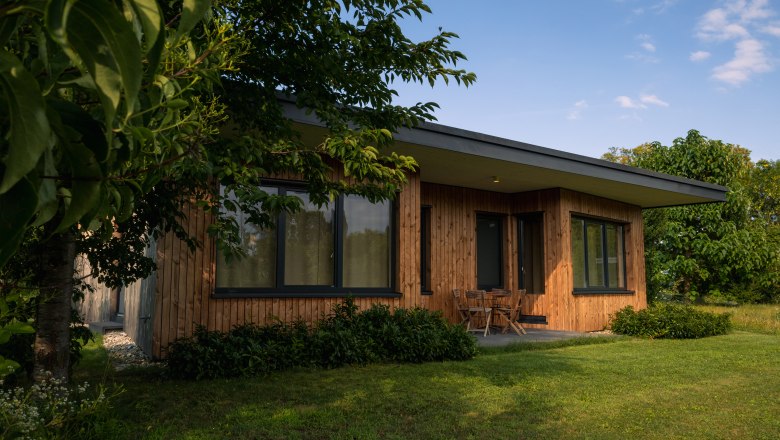 Chaty Grafenegg, © Niederösterreich Werbung / Maximilian Pawlikowsky Moderný drevený dom s veľkými oknami, obklopený stromami a trávnikom.