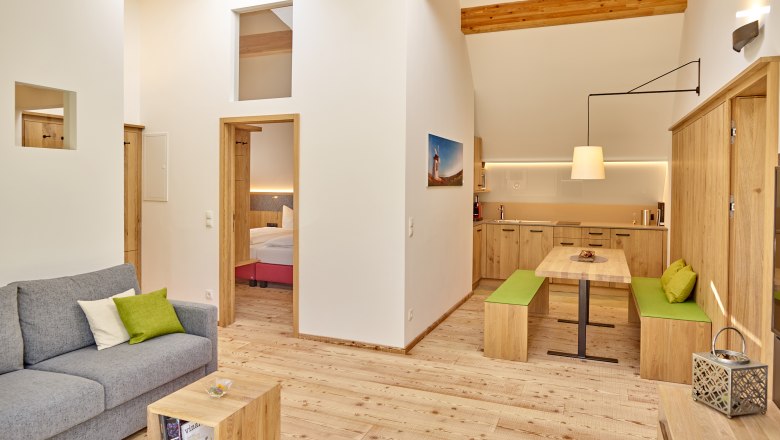 Weinviertler Kellerstöckl, © Weingut Hindler Moderná obývacia izba s dreveným nábytkom, sivou pohovkou a otvorenou kuchyňou.