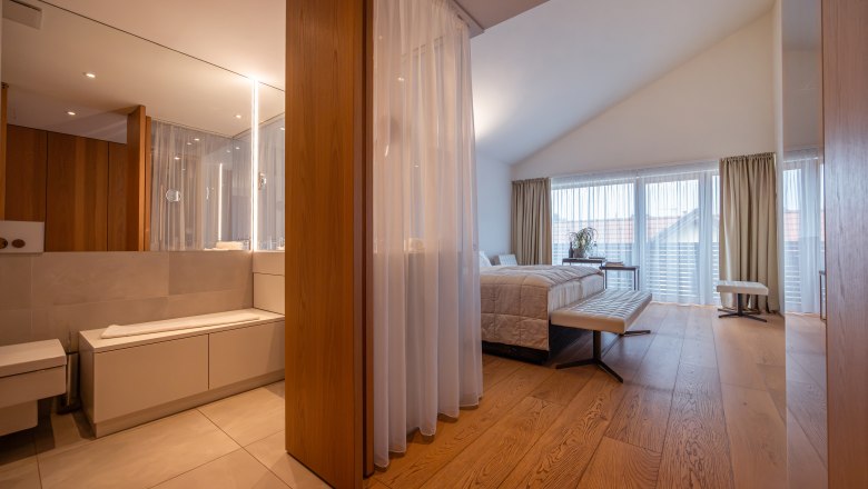 MÖRWALD, Relais Chateaux Hotel am Wagram, © Niederösterreich Werbung / Maximilian Pawlikowsky Moderná hotelová izba s drevenou podlahou, veľkou posteľou a kúpeľňou so zrkadlom.