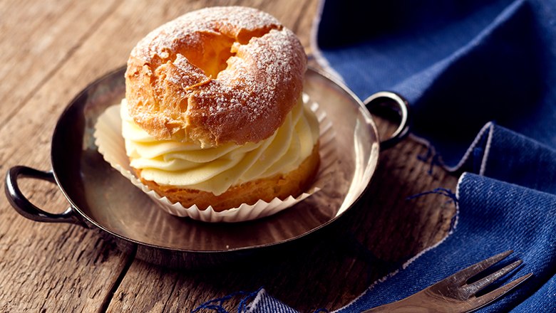 A filled choux pastry ring in a small pan, next to it a blue cloth and a fork., © Sooo gut schmeckt die Bucklige Welt/ Viktoria Kornfeld A filled choux pastry ring in a small pan, next to it a blue cloth and a fork., © Sooo gut schmeckt die Bucklige Welt/ Viktoria Kornfeld