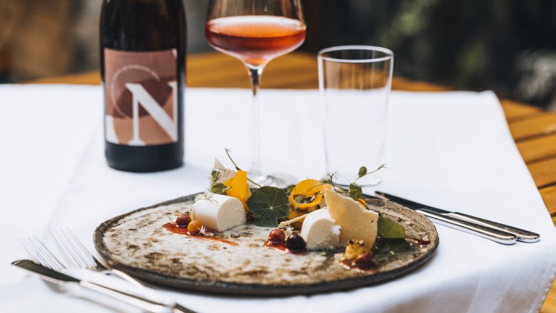 Naše vlastné víno, © Niederösterreich Werbung/David Schreiber Tanier so syrom a prílohou, pohár ružového vína a fľaša vína na stole.