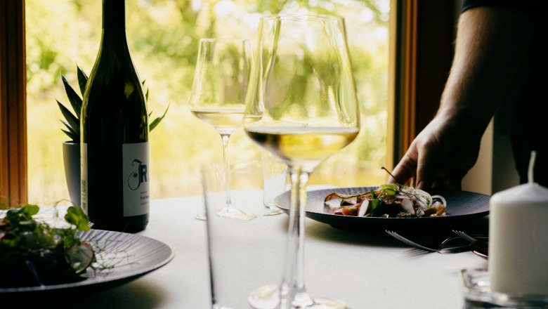 Reštaurácia vo vinárstve Johnneshof Reinisch, © Julius Hirtzberger Položený stôl s fľašou vína, pohármi a tanierom s jedlom v reštaurácii.