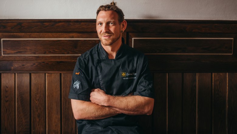 Prenajímateľ Michael Schindler, © Niederösterreich Werbung/Daniela Führer Muž v čiernom kuchárskom saku sedí pred drevenou stenou.