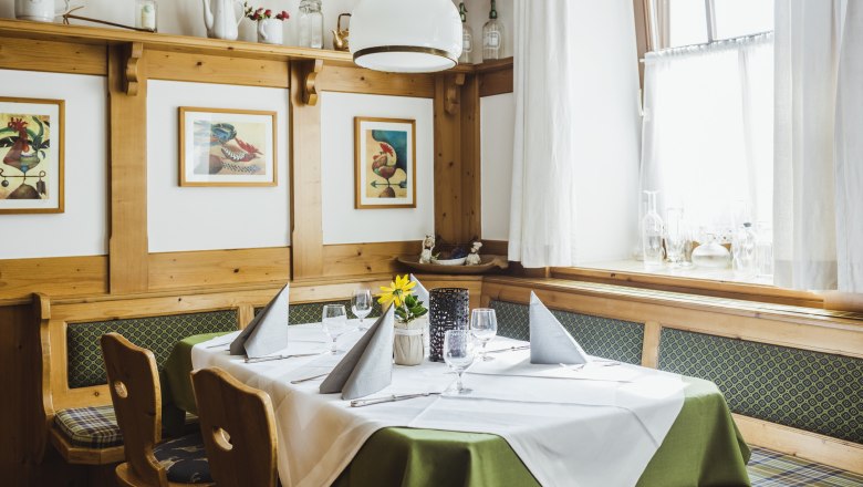 Salón so stolom pre štamgastov, © Niederösterreich Werbung/David Schreiber Útulný salónik s dreveným nábytkom, prestretým stolom a obrazmi na stene.