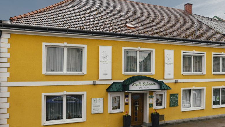 Taverna s mnohými bio produktmi, © Niederösterreich Werbung/David Schreiber Žltý domček pre hostí so zelenou markízou a niekoľkými oknami.