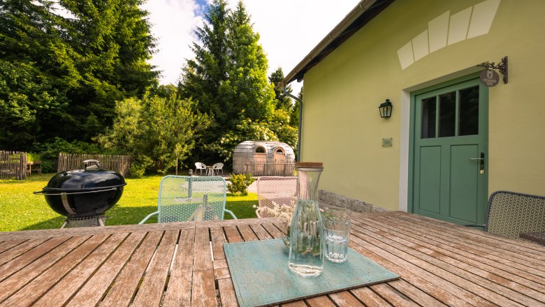 Dovolenka v hoteli BAHNhof, © Niederösterreich Werbung / Maximilian Pawlikowsky Záhrada s dreveným stolom, stoličkami, grilom a saunou v tvare suda.