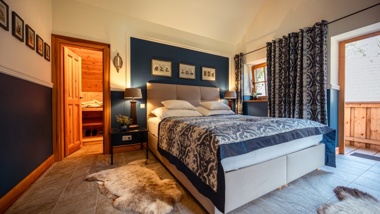 Lesnícka chata Langschlägerwald, © Niederösterreich Werbung / Maximilian Pawlikowsky Útulná spálňa s manželskou posteľou, modrými stenami a drevenými prvkami, susediaca so saunou.