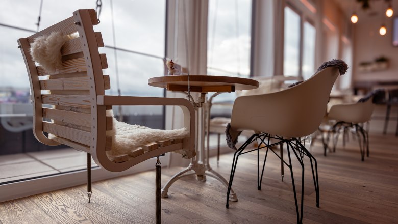 Alfred, © Niederösterreich Werbung / Maximilian Pawlikowsky Pohľad do interiéru kaviarne s modernými stoličkami a dreveným stolom, v pozadí veľké okná.