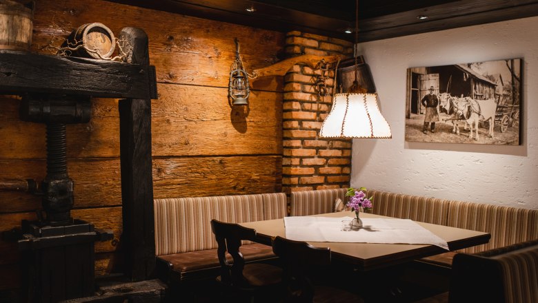 Posaďte sa v útulnej reštaurácii, © Niederösterreich Werbung/Daniela Führer Útulný salónik s drevenými stenami, rohovou lavicou, stolíkom s kvetmi a lampou. Na stene visí historická fotografia.