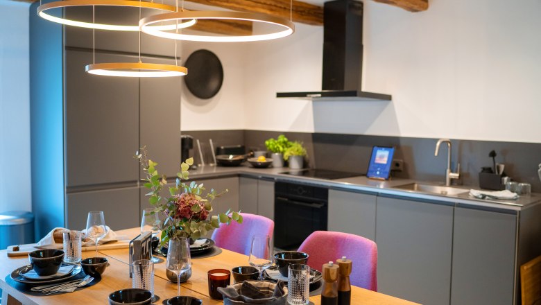 Chaty a miesta plné ZÁZRAKOV - Weidehaus De Luxe, © WUNDERVOLL eben Moderná kuchyňa s jedálenským stolom pre štyri osoby a štýlovým osvetlením.