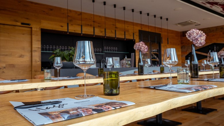 Vínny domicil Hagn, © Niederösterreich Werbung / Maximilian Pawlikowsky Pohľad do interiéru moderného vinárskeho domu s položenými stolmi, pohármi na víno a dekoráciami.