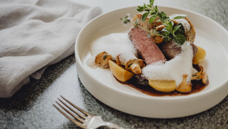 Dva druhy saßwaldskej zveriny, makové pirohy, © Niederösterreich Werbung/Rita Newman Gurmánske jedlo so zverinou, servítkovou knedľou, hubami a penou na bielom tanieri.