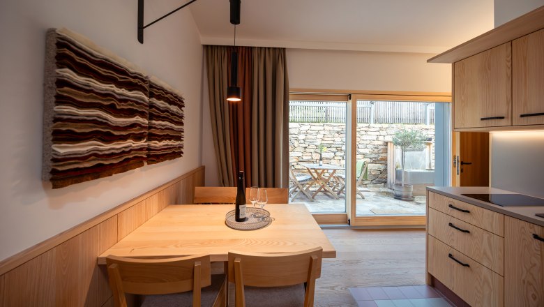 Weinviertler Kellerstöckl Vinárstvo Hindler, © Niederösterreich Werbung / Maximilian Pawlikowsky Pohľad do interiéru modernej jedálne s dreveným nábytkom a umeleckými dielami na stene, pohľad na terasu cez sklenené dvere.