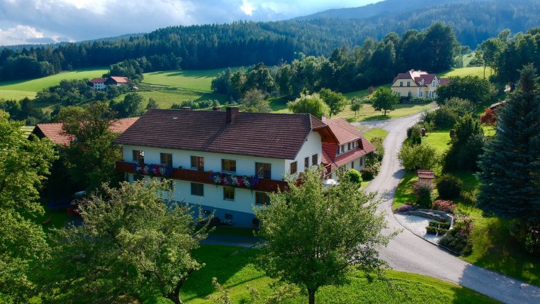 ...uprostred prírody., © Familie Rosinger Vidiecka krajina s veľkým domom, obklopená stromami a lúkami, pod zamračenou oblohou.