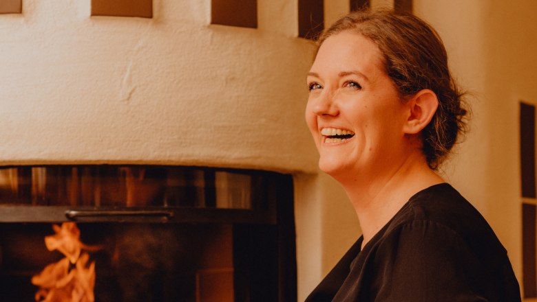 Statkárka Eva Maria Reisenbauerová, © Niederösterreich Werbung/Klaus Engelmayer Žena sa usmieva pred krbom s horiacim ohňom.