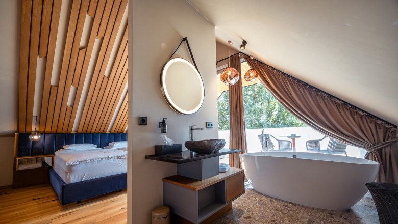 Vínny domicil Hagn, © Niederösterreich Werbung / Maximilian Pawlikowsky Moderná hotelová izba s dreveným stropom, voľne stojacou vaňou a balkónom.