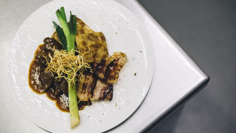 Hovädzia pečienka z Alpenvorlandu Beiried, © Niederösterreich Werbung/David Schreiber Tanier s hovädzou pečienkou, zemiakovým gratinovaním, pórom a chrumkavou cibuľkou na kovovom povrchu.