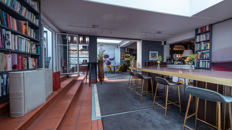 Relais & Chateaux MÖRWALD Hotel am Wagram, © Niederösterreich Werbung / Maximilian Pawlikowsky Pohľad do interiéru modernej hotelovej izby s policami na knihy, vysokými stolmi a barovými stoličkami.