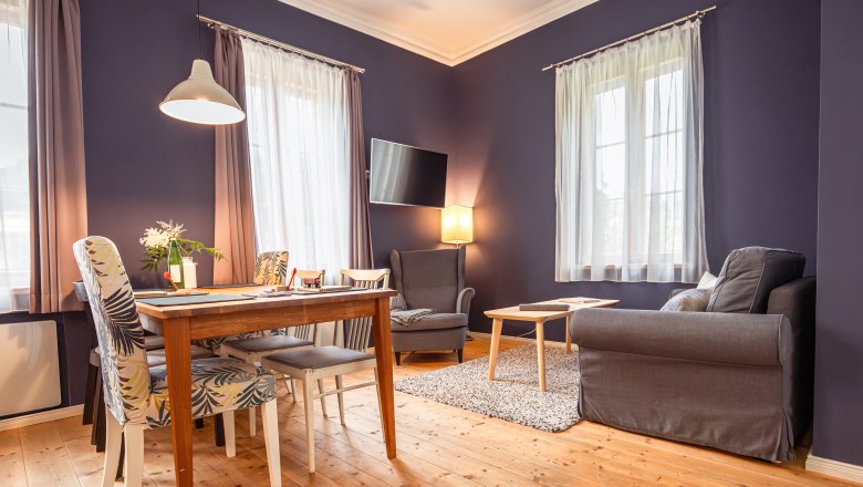 Dovolenka v hoteli BAHNhof, © Niederösterreich Werbung / Maximilian Pawlikowsky Útulná obývacia izba s drevenou podlahou, jedálenským stolom, stoličkami, kreslom a pohovkou.