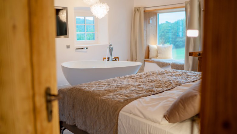 Chaty a miesta plné ZÁZRAKOV - Weidehaus De Luxe, © WUNDERVOLL eben Pohľad do interiéru luxusnej spálne s voľne stojacou vaňou, veľkou posteľou a okenným sedadlom s vankúšmi.