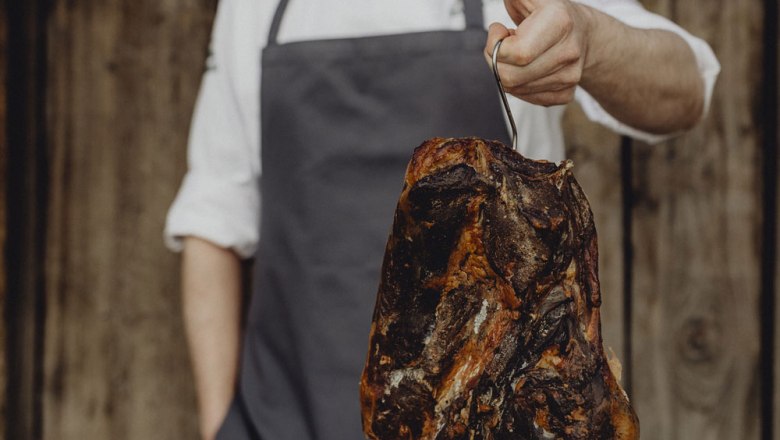 Domáca údená šunka Emmerberger, © Niederösterreich Werbung/Sophie Menegaldo Osoba držiaca údenú šunku na háčiku.