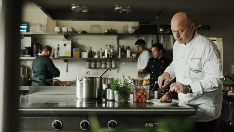 Manfred Hausgnost v kuchyni, © Niederösterreich Werbung/Michael Reidinger Kuchári pracujú v profesionálnej kuchyni, jeden krája mäso.