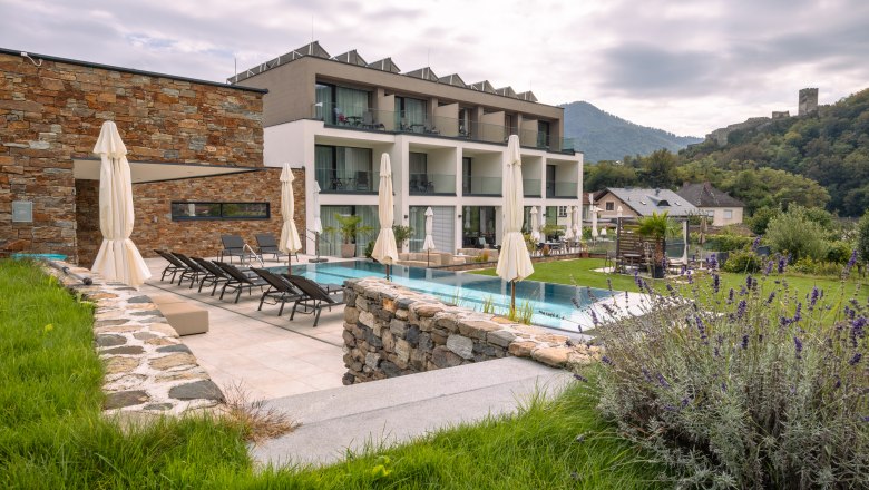 Boutique hotel WeinSpitz, © Niederösterreich Werbung / Maximilian Pawlikowsky Exteriérový pohľad na moderný butikový hotel s bazénom a ležadlami, obklopený zelenou krajinou a kopcami.