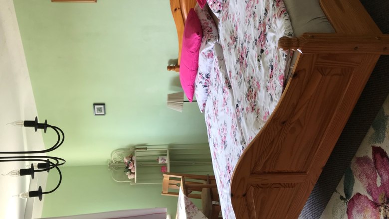 Sp&aacute;lňa s manželskou posteľou, zelen&yacute;mi stenami, kvetinovou posteľnou bielizňou, stolom so stoličkami, z&aacute;vesmi a lustrom.