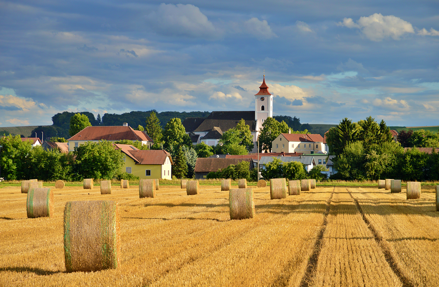 Krajina s balíkmi slamy a kostolom v Michelhausene.