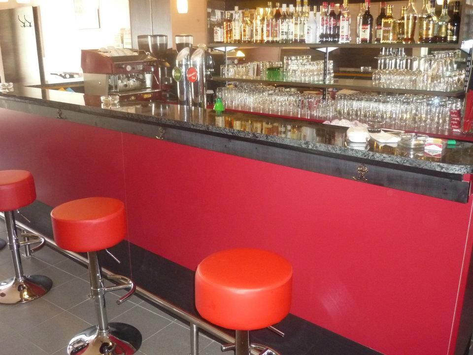 Pohľad do interiéru baru s červenými stoličkami a dobre zásobeným pultom.