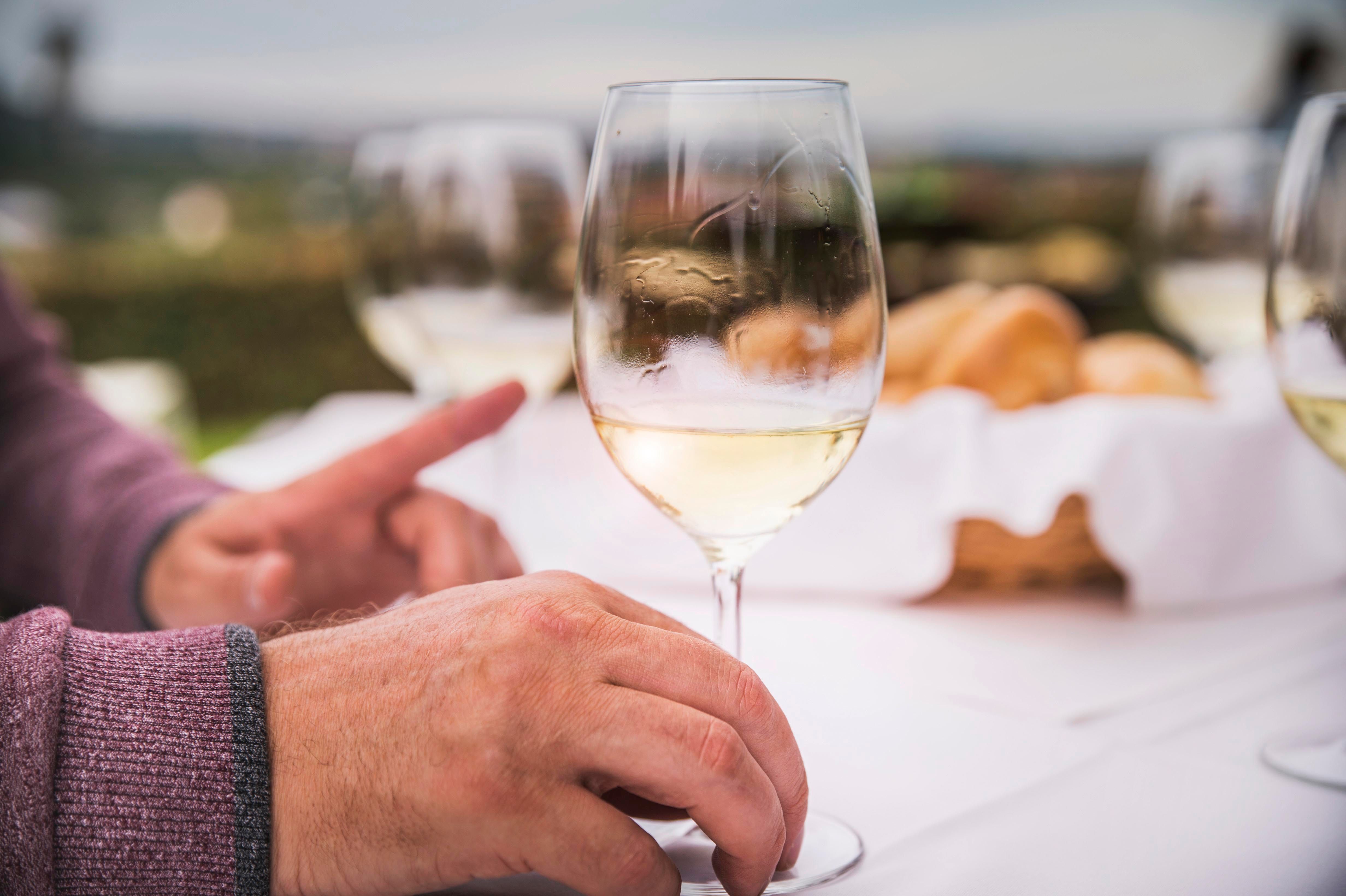 Detailný záber na ruky s pohárom na víno na položenom stole v exteriéri.