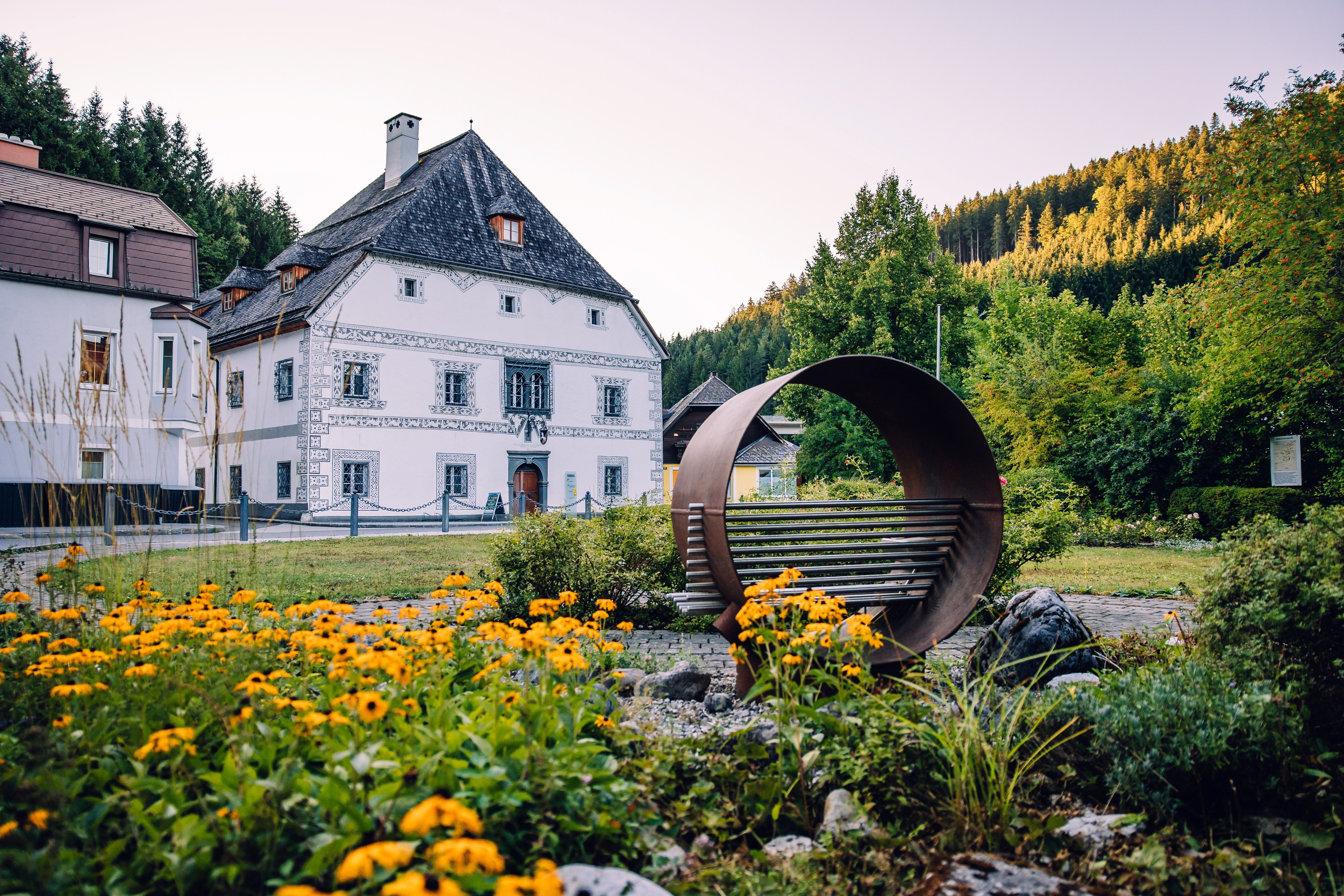 Dom Amonhaus v Lunz am See, s počúvacím kreslom v popredí a kvetinovými záhonom pred historickou budovou.