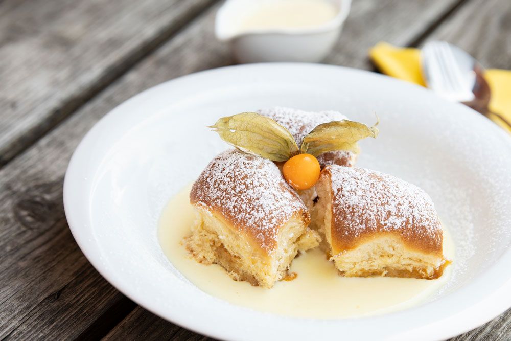 Tri Buchteln s práškovým cukrom a physalis na vanilkovej omáčke na bielom tanieri.