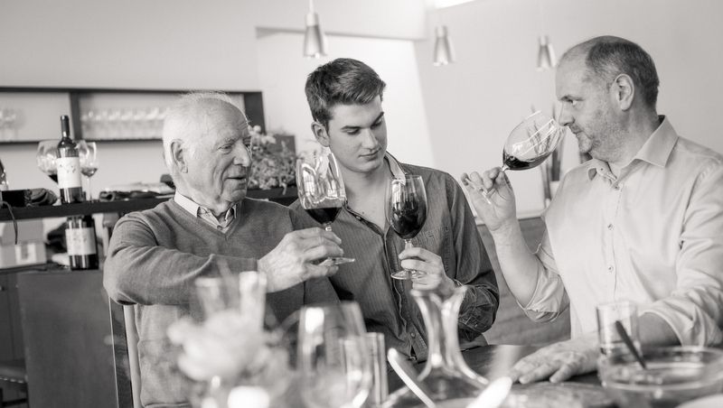 Traja muži si pri stole cinknú pohárom vína.