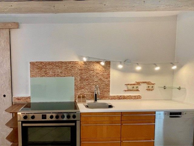 Moderná kuchyňa so sporákom, drezom a umývačkou riadu pred mozaikovou obkladovou stenou.