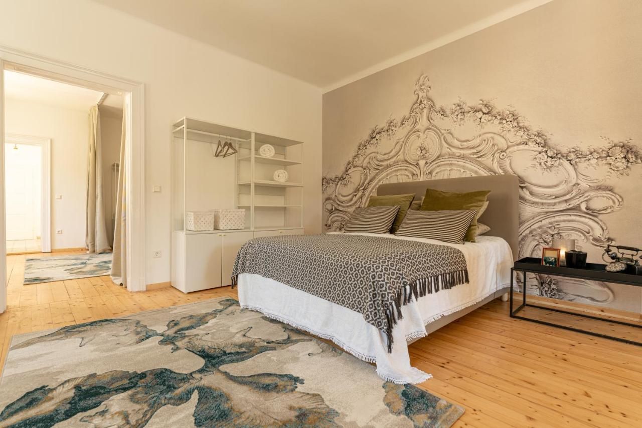 Štýlovo zariadená spálňa s veľkou posteľou, ozdobnými vankúšmi, kobercom a umeleckým dizajnom stien.