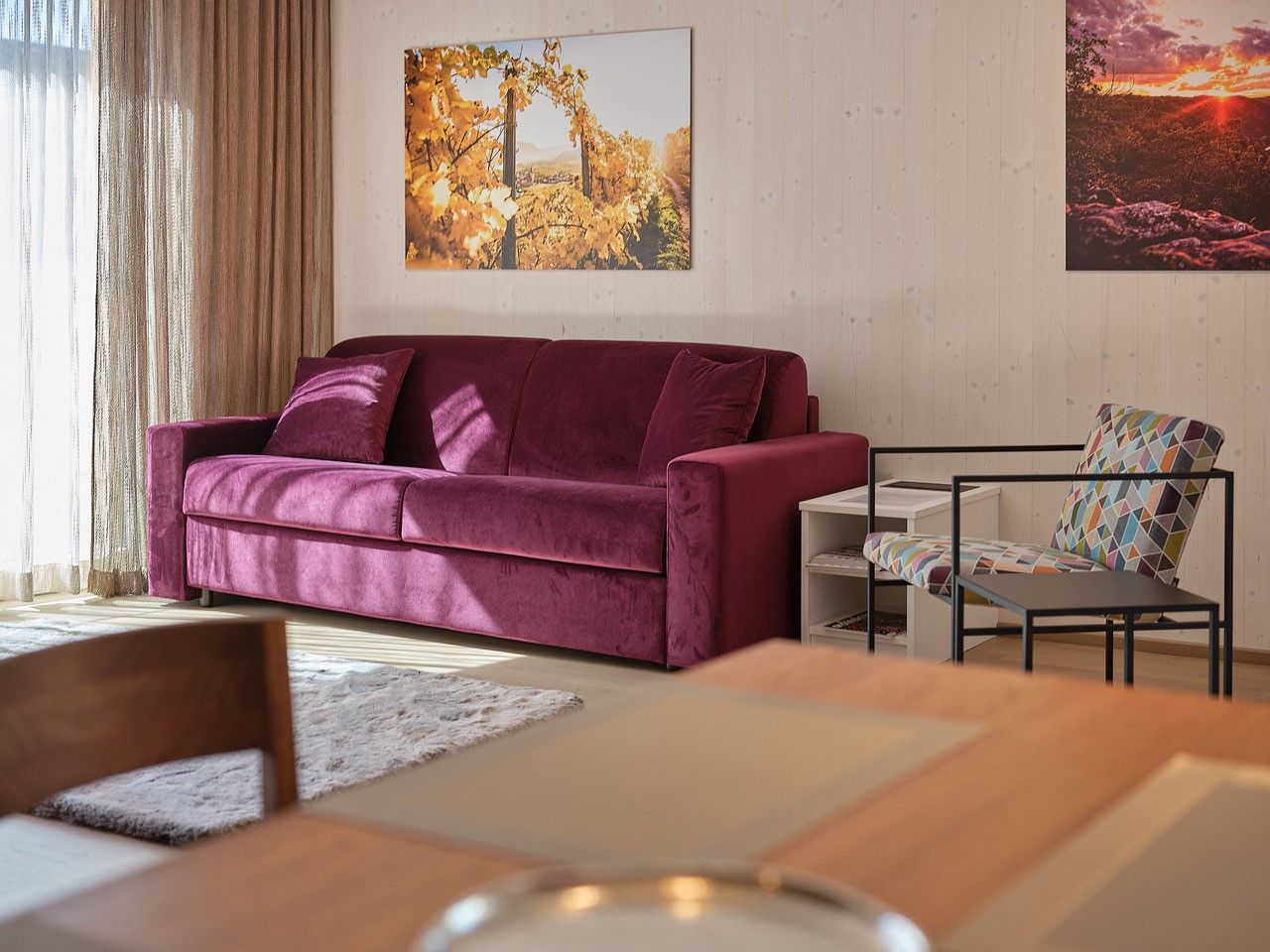 Obývacia izba s fialovou pohovkou, farebným kreslom a nástennými maľbami.