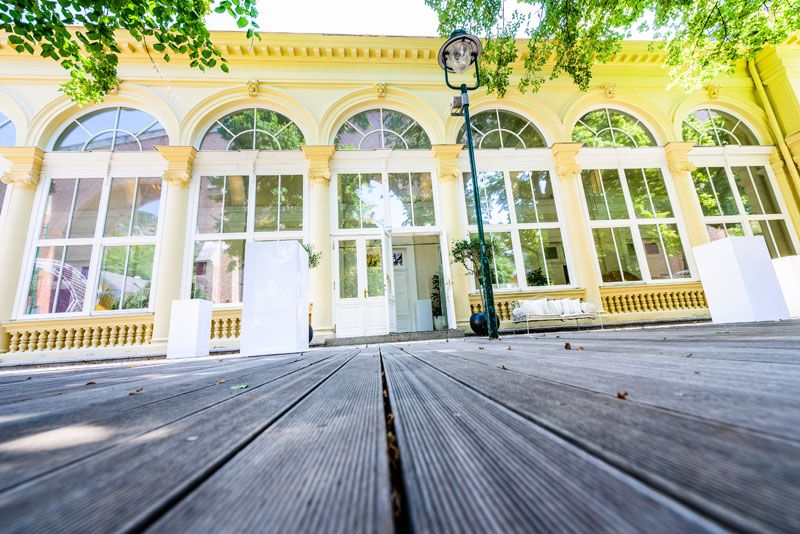 Exteriérový pohľad na Kursalon Mödling s veľkými oknami a drevenou podlahou.