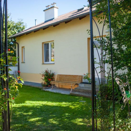 Žltý domček so záhradnou lavičkou a kvetmi v popredí.