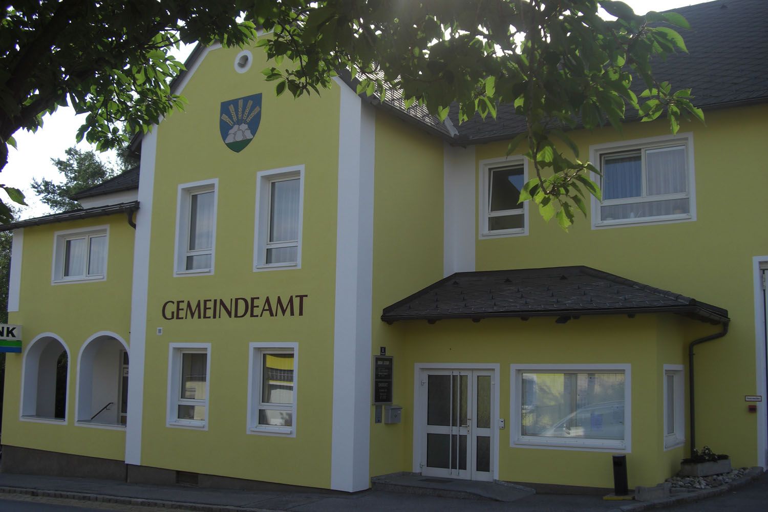 Žltá budova s nápisom "GEMEINDEAMT" a erbom nad ňou.
