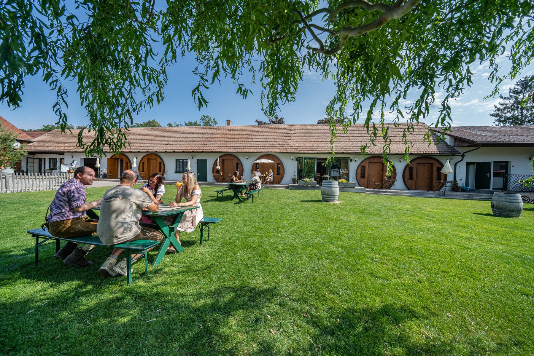 Ľudia sedia pri stole na trávniku pred budovou s okrúhlymi dverami.