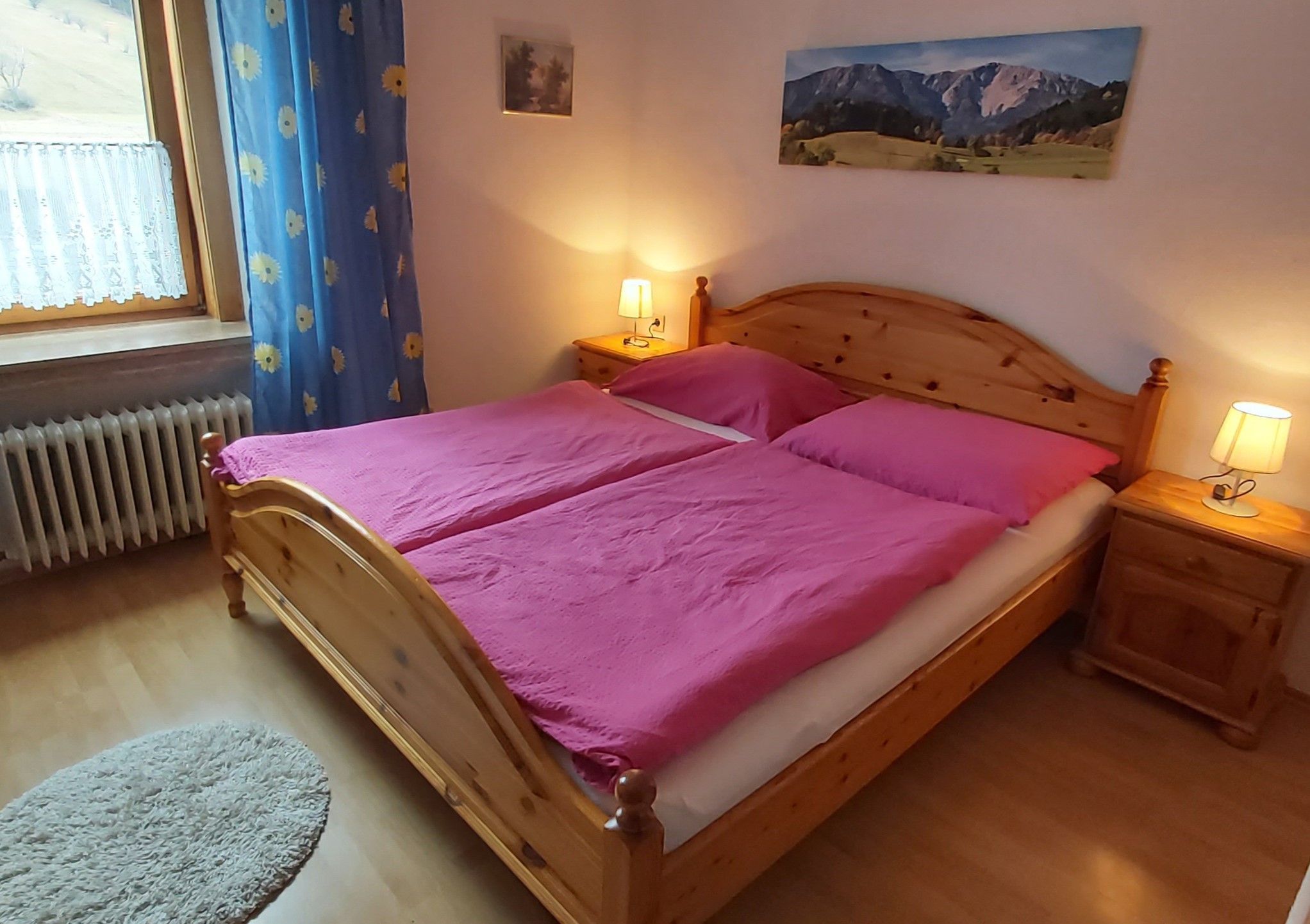 Útulná dvojlôžková izba s drevenou posteľou, ružovou posteľnou bielizňou a nočnými stolíkmi s lampami.