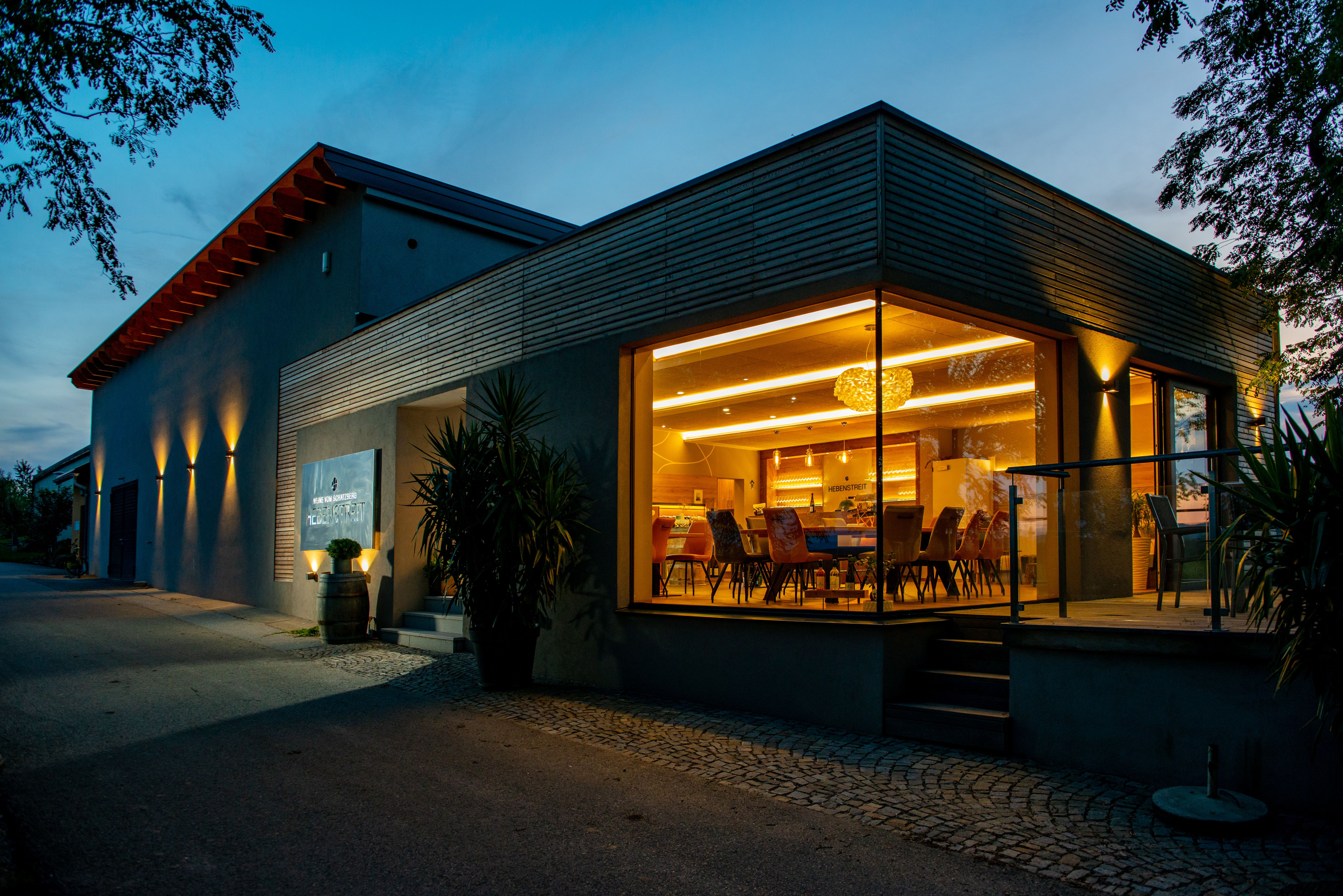 Moderná budova so skleneným priečelím a vnútorným osvetlením za súmraku.