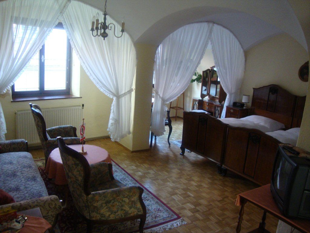 Útulná izba pre hostí so starožitným nábytkom, manželskou posteľou, kreslami a malou TV. Priestor na spanie je oddelený závesmi.